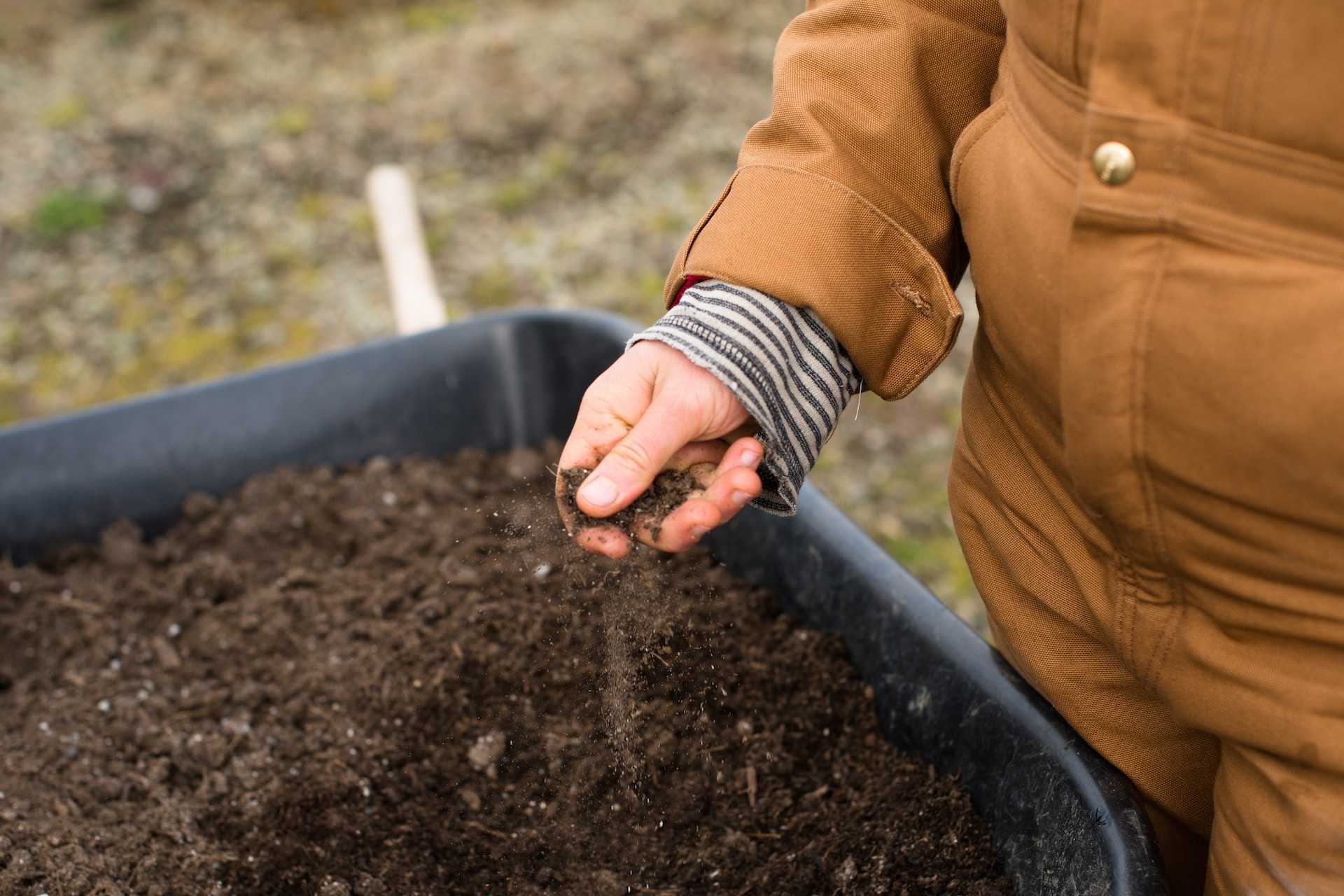 The hand of a farmer in a brown boiler suit which is filled with soil. 